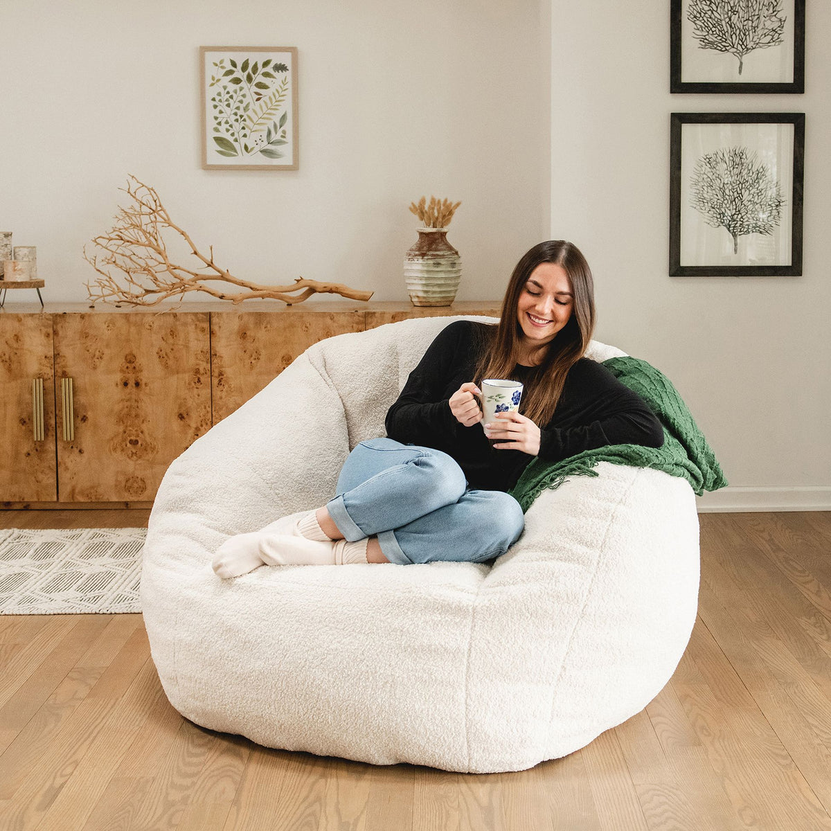 Girl holding a coffee cup on a white cloud-like chair in the living room 