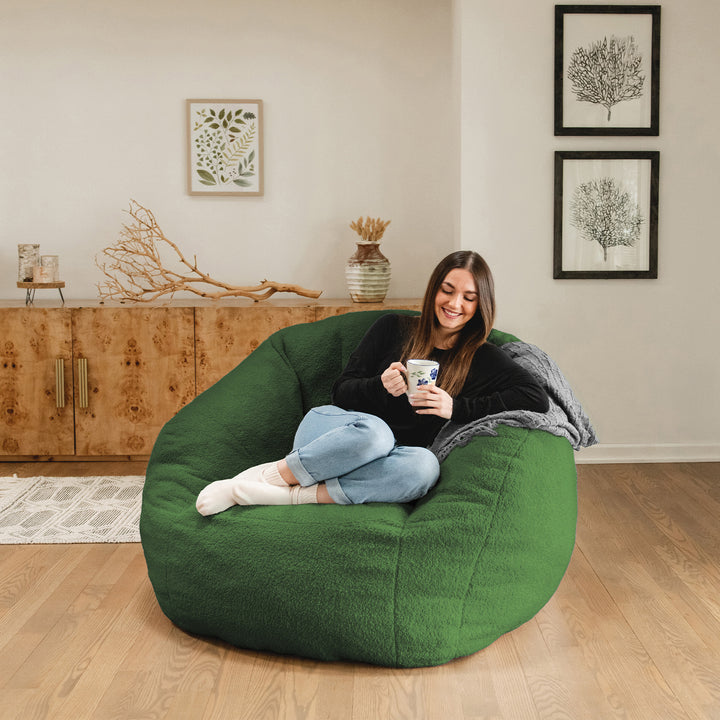 Woman sitting on a green bean bag chair in a room with wooden floor and wall decorations. 