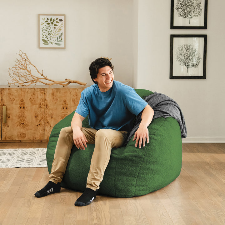 Man sitting on a green bean bag chair in a room with wooden floor and wall decorations. 