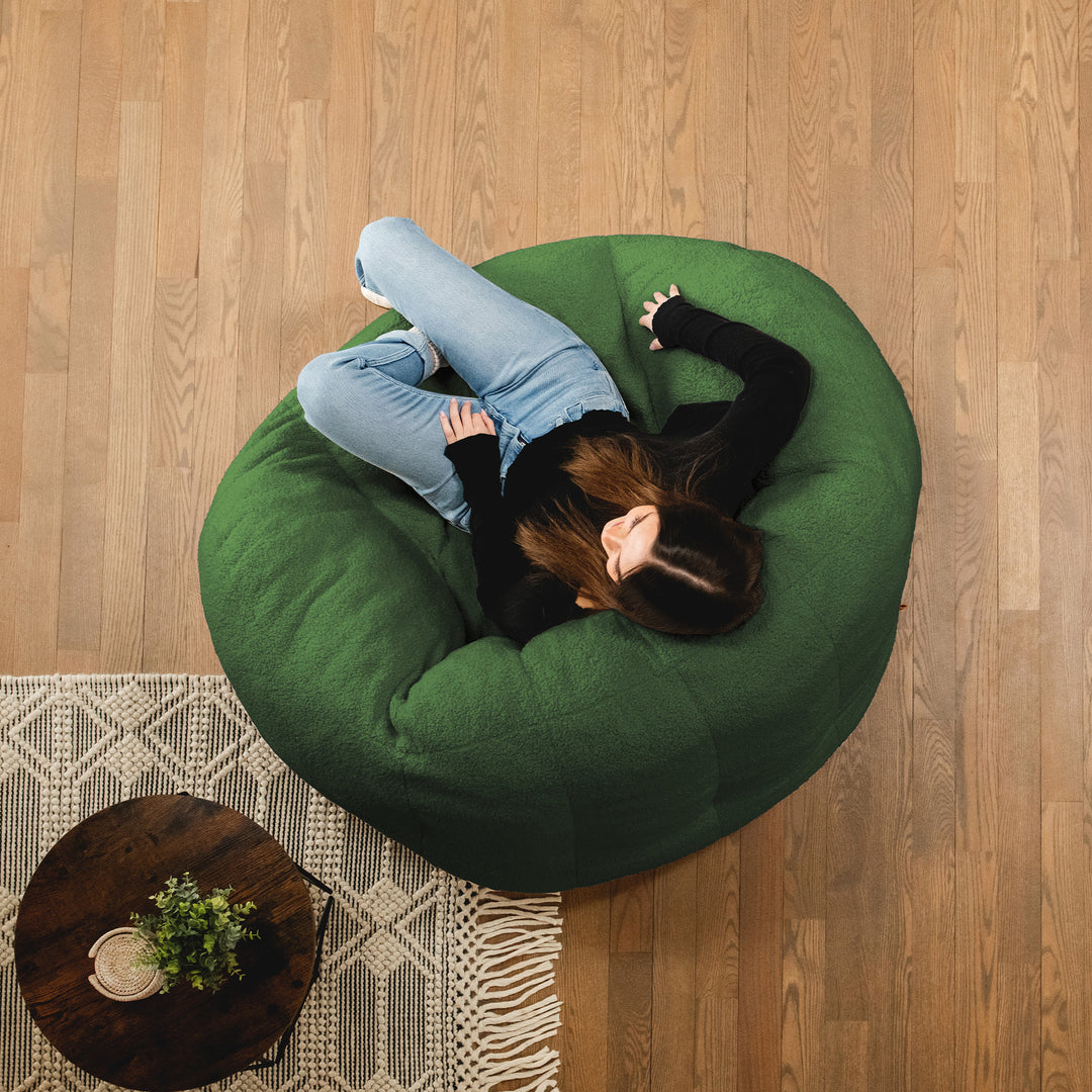 Person lying on a green bean bag chair in a room with wooden flooring and a small table. 