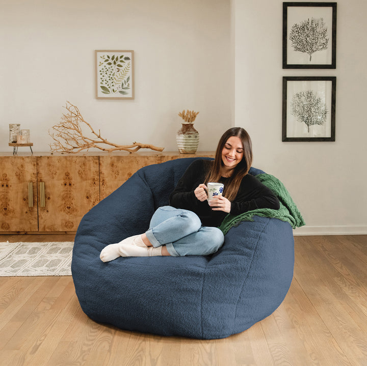 Woman sitting on a large blue bean bag chair in a living room, holding a mug. 