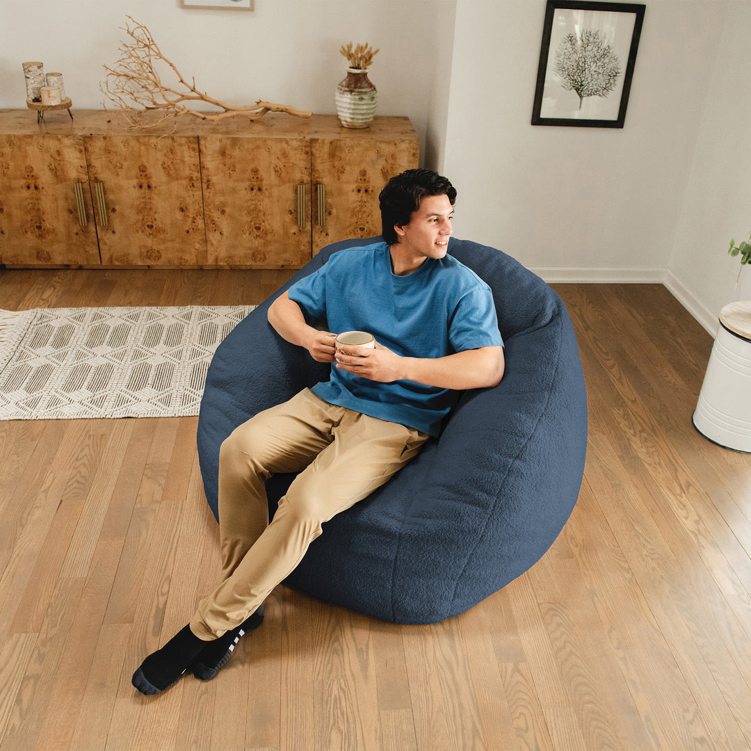 Man sitting on a blue bean bag chair in a living room. 