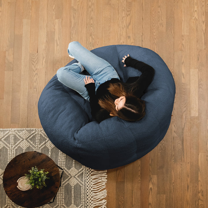 Person lying on a blue bean bag chair in a room with wooden flooring and a small table. 