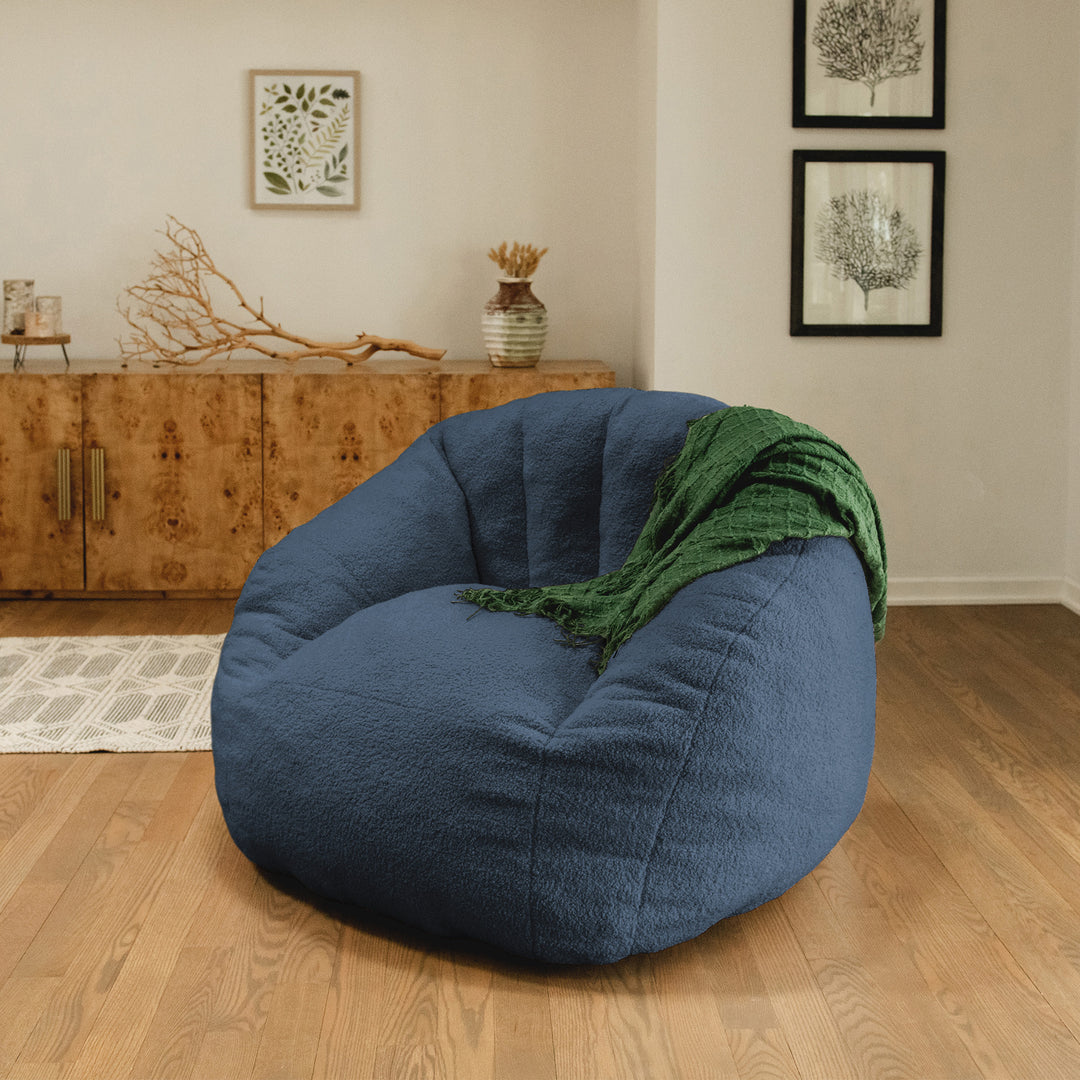 Blue bean bag chair with a green blanket in a room with wooden flooring and a wooden cabinet. 