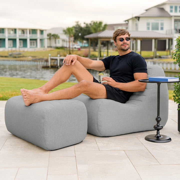 Man sitting on a gray outdoor sofa with a drink, surrounded by a waterfront view. #color_port-gray-outdoor-performance-linen