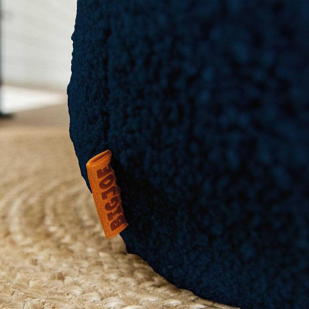 Close-up of a textured blue cushion with an orange tag on a beige carpet. #color_deep-blue-teddy-boucle