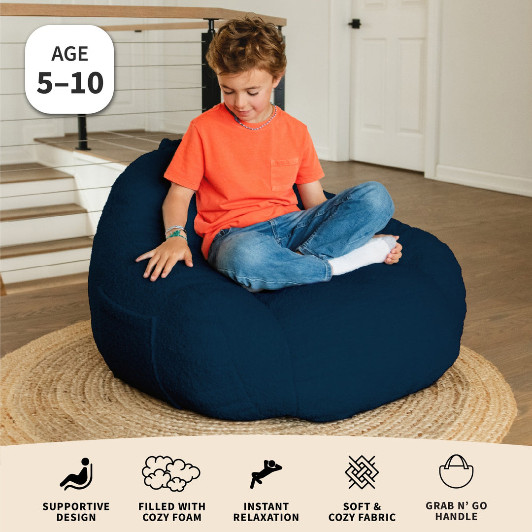 Boy sitting on a blue bean bag chair with features displayed age 5-10 #color_deep-blue-teddy-boucle