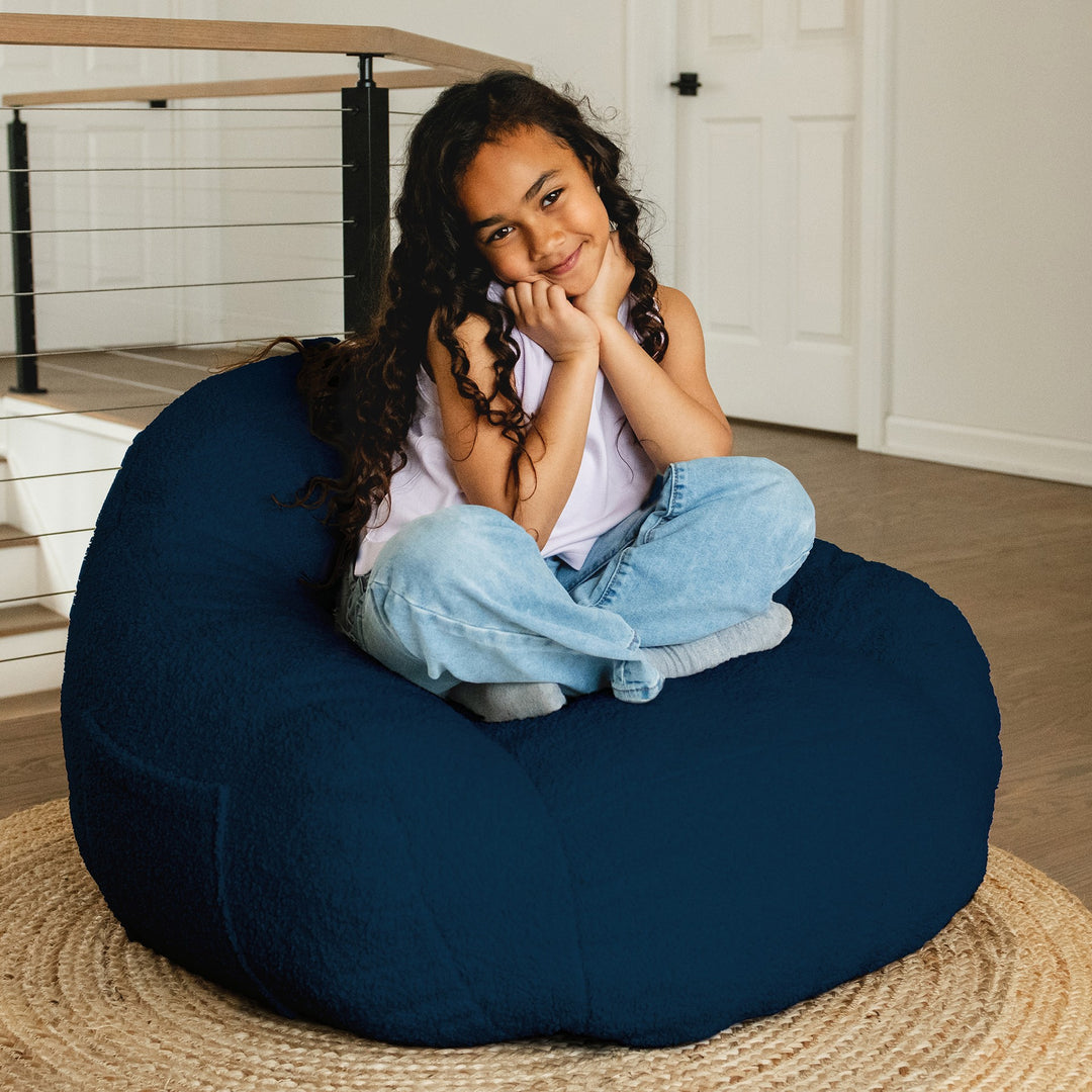 Child sitting on a navy bean bag chair in a home setting #color_deep-blue-teddy-boucle