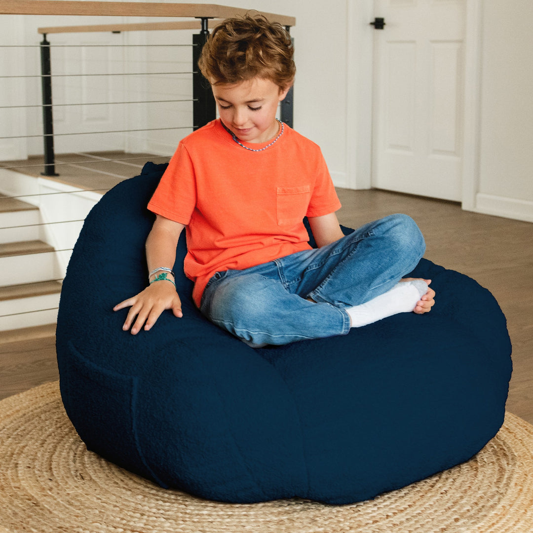 Child sitting on a navy bean bag chair indoors #color_deep-blue-teddy-boucle