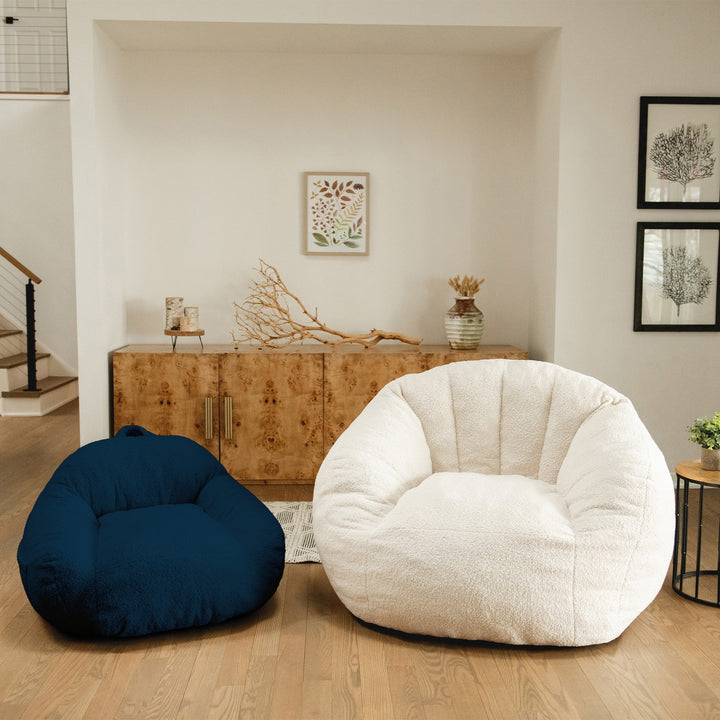 Two bean bags, one blue kids sized and one white adult sized, in a living room setting with a wooden cabinet and decorative elements. #color_deep-blue-teddy-boucle