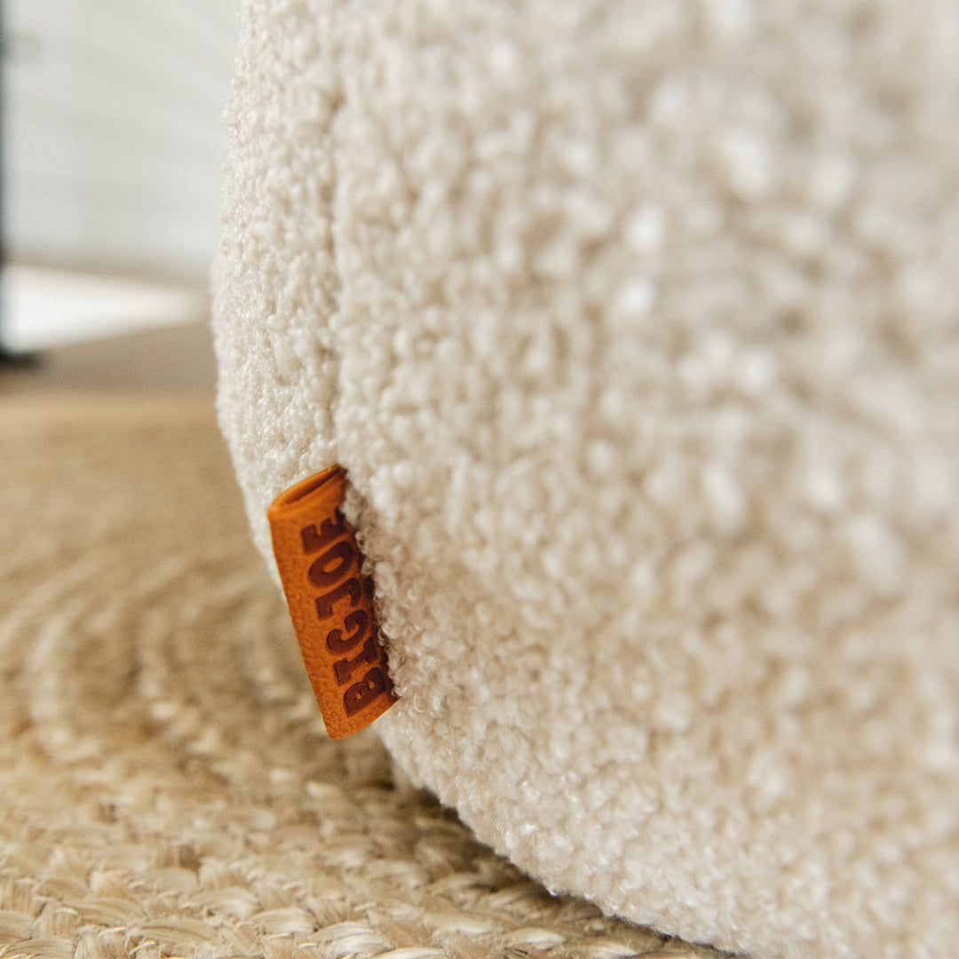 Close-up of a textured beige beanbag with a brand tag on a carpeted floor. #color_icing-teddy-boucle