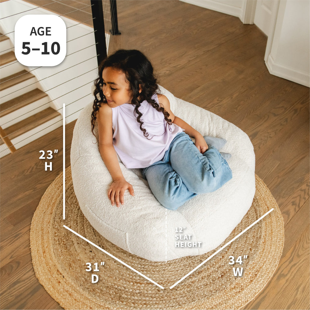 Child sitting on a bean bag chair with dimensions displayed #color_icing-teddy-boucle