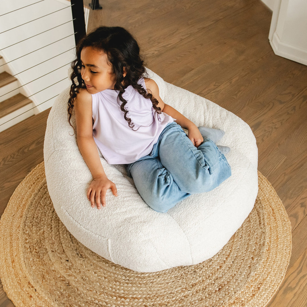 Child sitting on a white bean bag chair in a home setting #color_icing-teddy-boucle