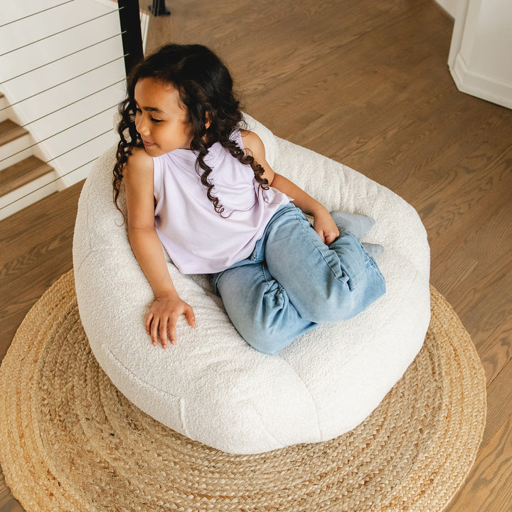 Child sitting on a white bean bag chair in a home setting #color_icing-teddy-boucle