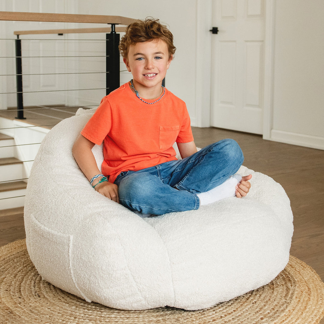 Child sitting on a large white bean bag chair indoors. #color_icing-teddy-boucle
