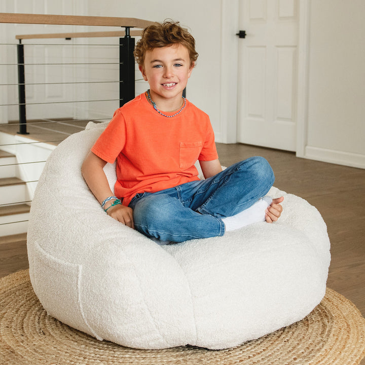 Child sitting on a large white bean bag chair indoors. #color_icing-teddy-boucle
