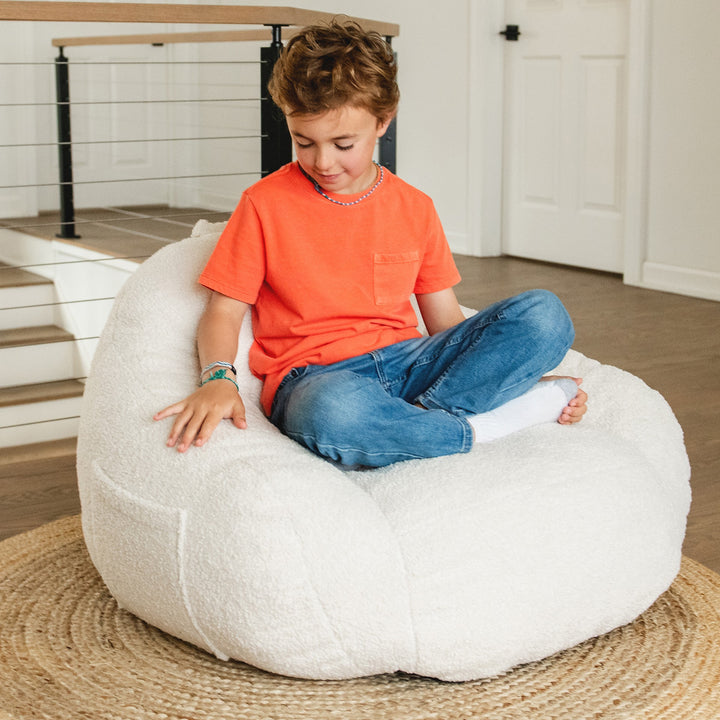Child sitting on a white bean bag chair indoors #color_icing-teddy-boucle
