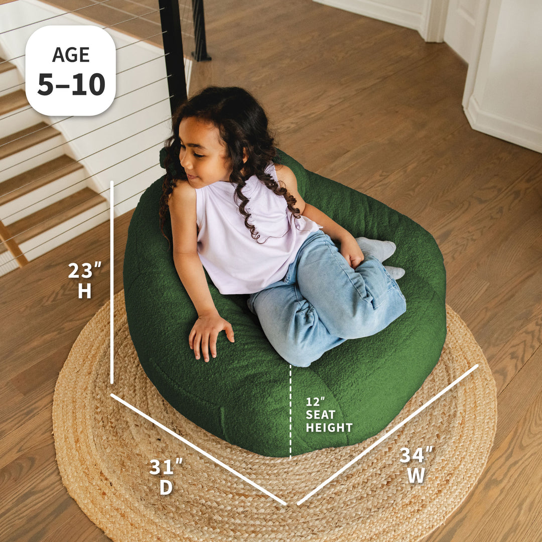Child sitting on a green bean bag chair with measurements displayed, on a wooden floor. 