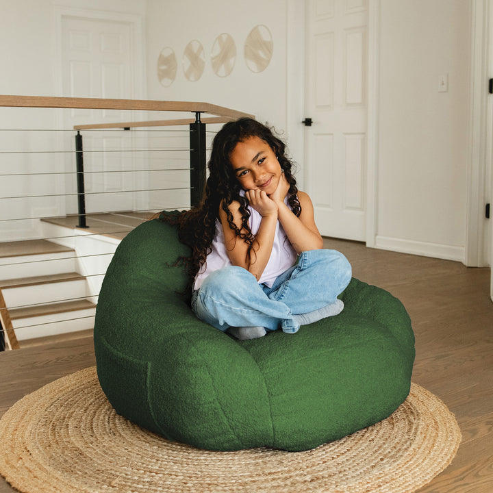 Young girl sitting on a green bean bag chair in a home setting. 