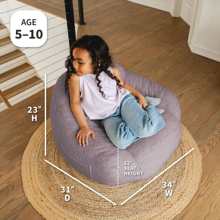 Child sitting on a bean bag chair with dimensions displayed, on a wooden floor. 
