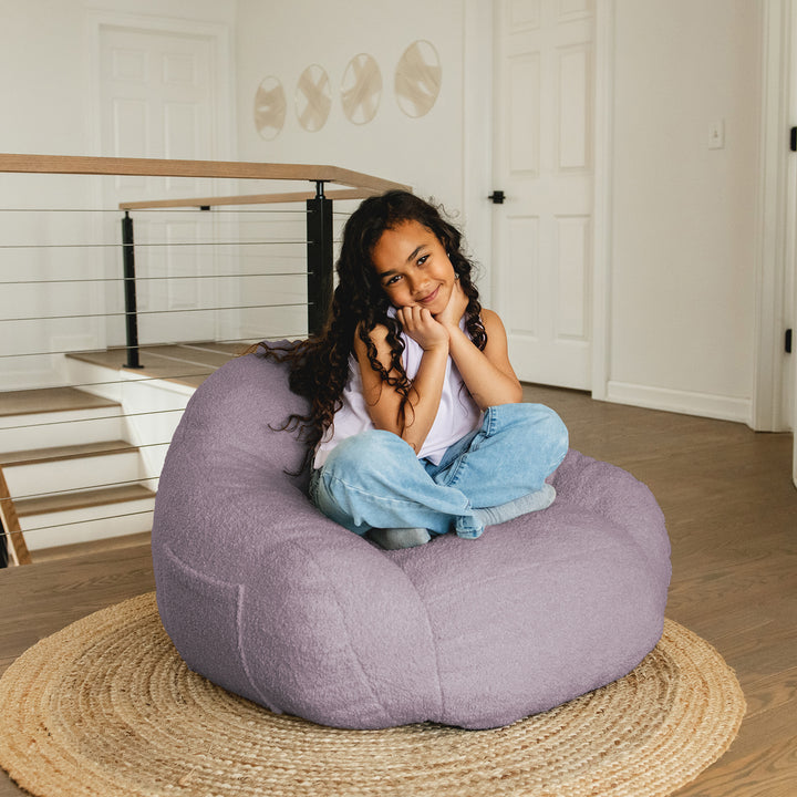 Child sitting on a large purple bean bag chair in a home setting. 