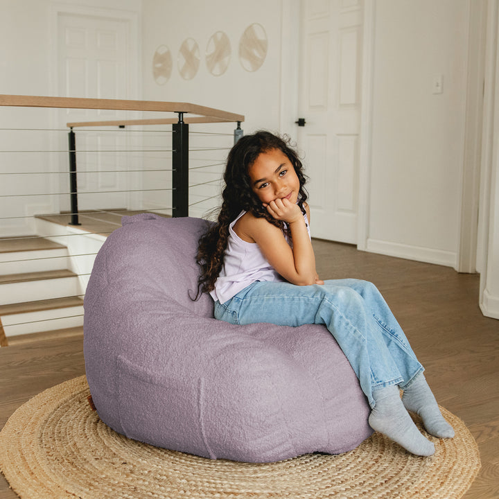 Young girl sitting on a purple bean bag chair in a home setting. 