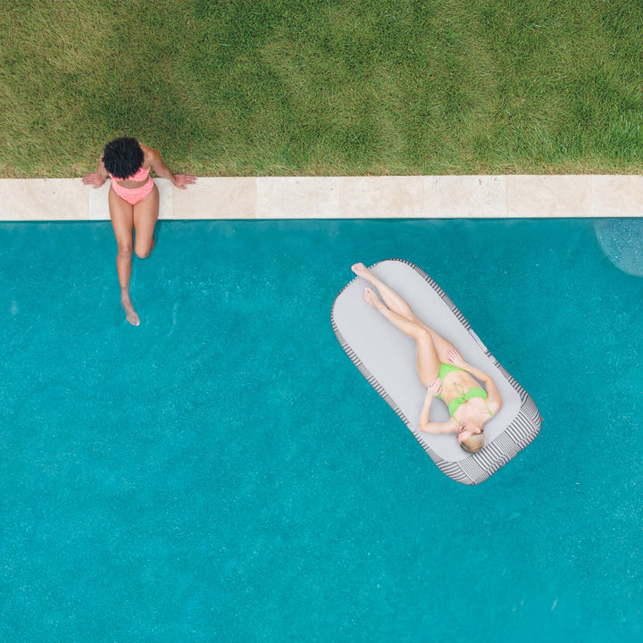 Two people by a pool, one standing and one lying on an inflatable raft. #color_shoreline-gray-stripe-olefin