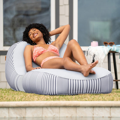 Woman in a bikini lying on a striped bean bag chair by a poolside. 