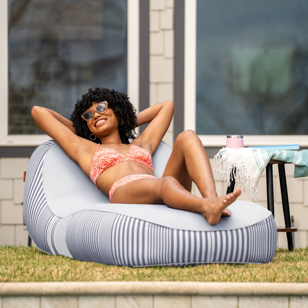 Woman in a bikini sitting on a striped bean bag chair outdoors. 