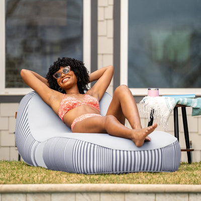 Woman in a bikini sitting on a striped bean bag chair outdoors. 