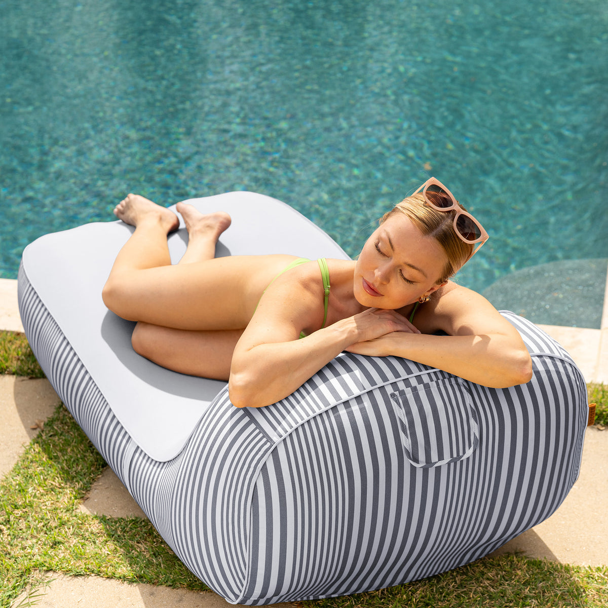 Woman relaxing on a striped inflatable pool float by a pool 