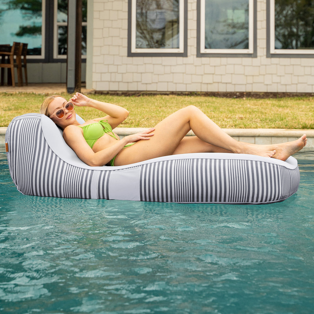 Woman lounging on a striped pool float in a pool with a house in the background #color_shoreline-gray-stripe-olefin