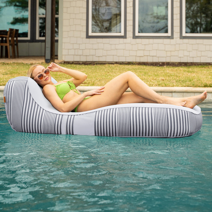 Woman lounging on a striped pool float in a pool with a house in the background #color_shoreline-gray-stripe-olefin