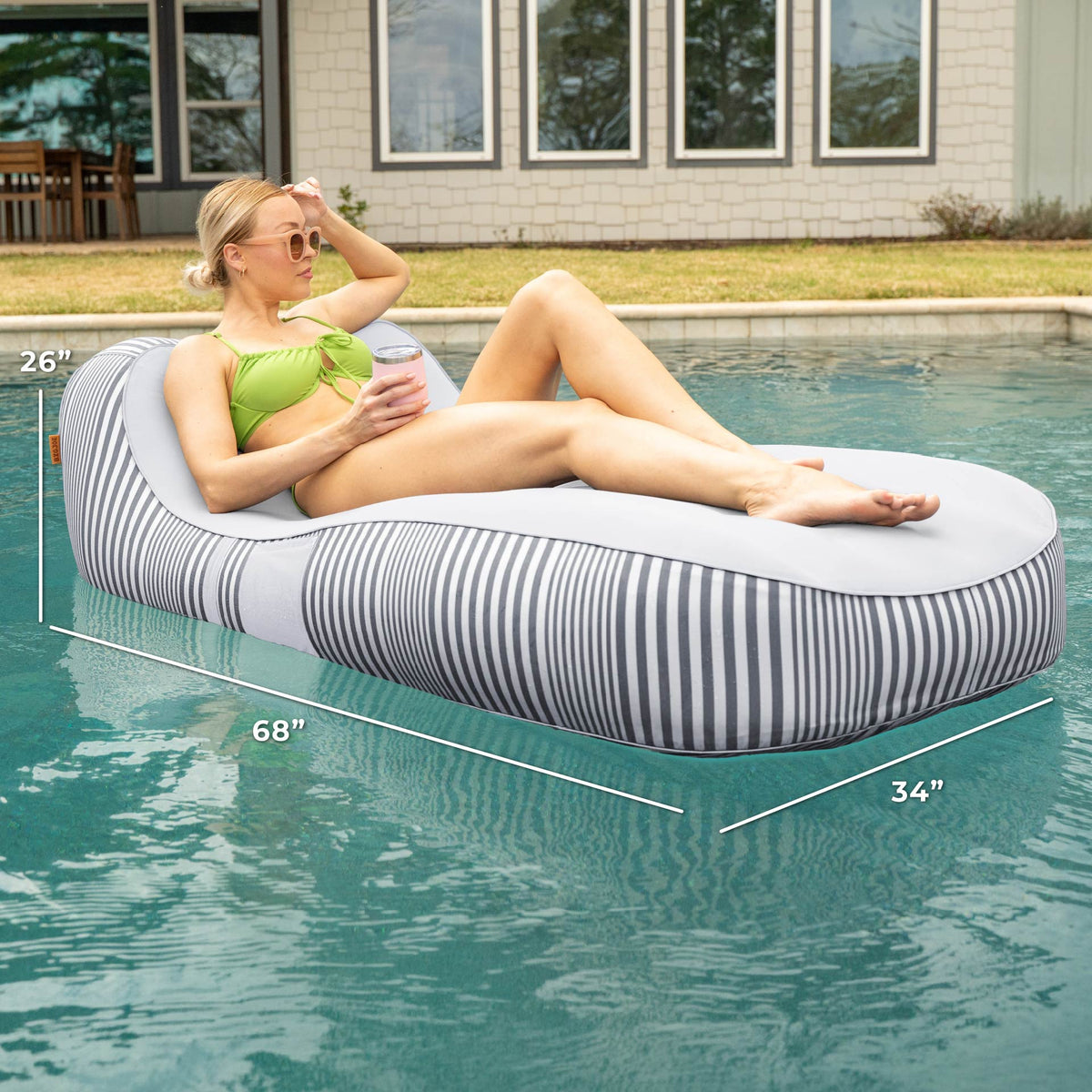 Woman lounging on a striped pool float with dimensions displayed, set against a poolside background. #color_shoreline-gray-stripe-olefin