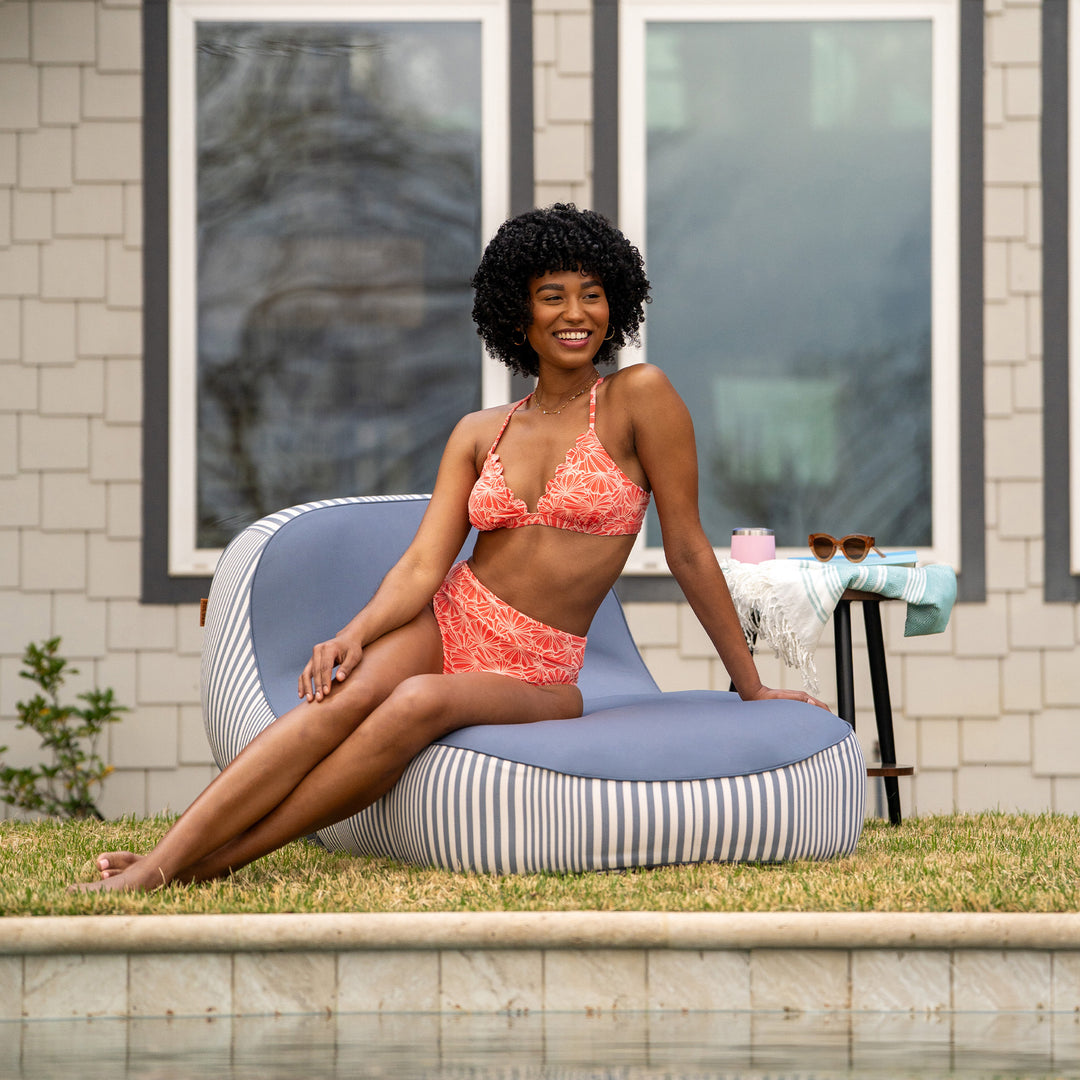 Woman in a pink bikini sitting on a striped bean bag by a pool #color_weekend-navy-stripe-olefin