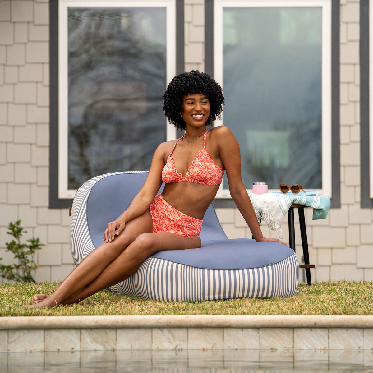 Woman in a pink bikini sitting on a striped bean bag by a pool 
