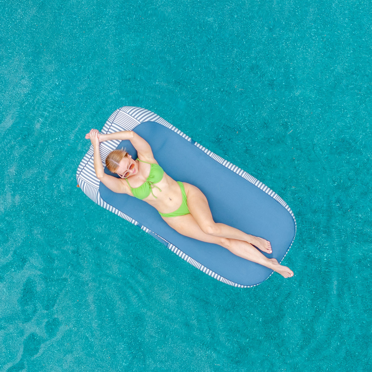 Woman lying on a blue inflatable pool float in clear blue water 