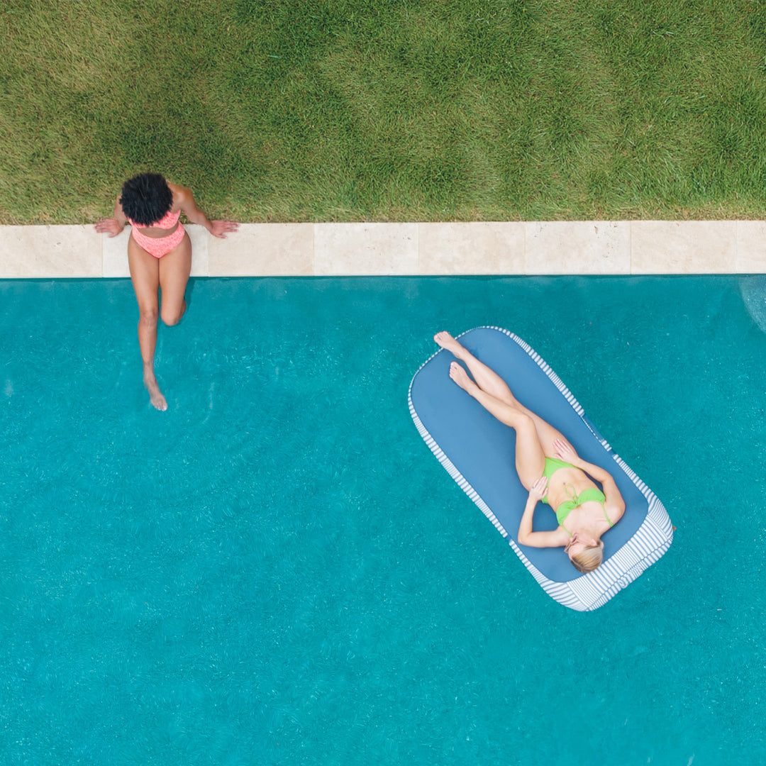 Two women by a pool, one standing and one lying on a floatie. #color_weekend-navy-stripe-olefin