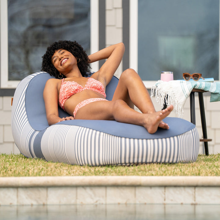 Woman in a pink bikini lying on a striped bean bag by a poolside. #color_weekend-navy-stripe-olefin