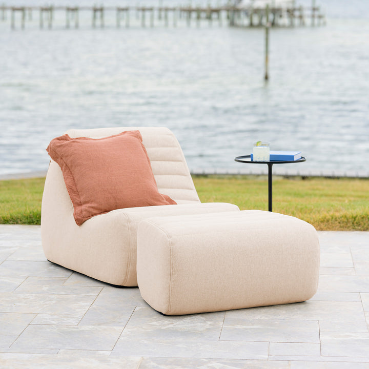 Beige outdoor chair with a pink pillow on a patio near a body of water. #color_sunlit-cream-outdoor-performance-linen