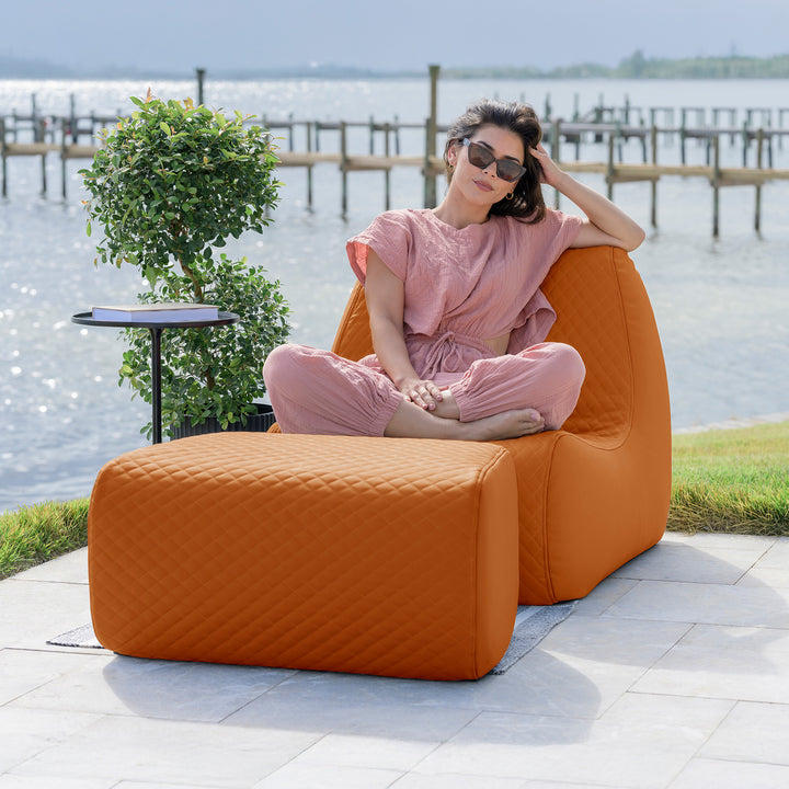 Woman sitting on an orange outdoor chair by a waterfront #color_honey-sand-outdoor-vegan-leather