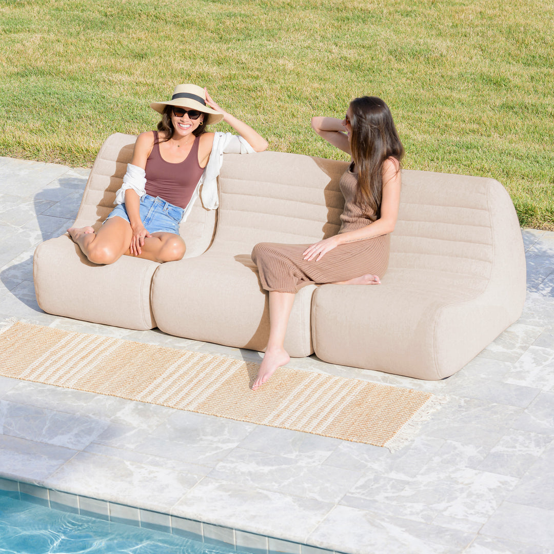Two women sitting on a sofa by a pool #color_sunlit-cream-outdoor-performance-linen