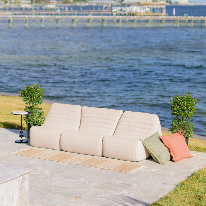 Beige outdoor sofa with colorful cushions on a patio by a waterfront. #color_sunlit-cream-outdoor-performance-linen