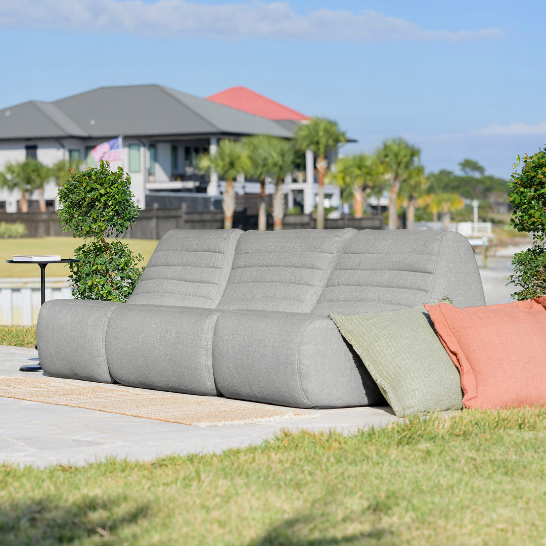 Gray outdoor sofa with colorful cushions on a patio with a house and trees in the background #color_port-gray-outdoor-performance-linen