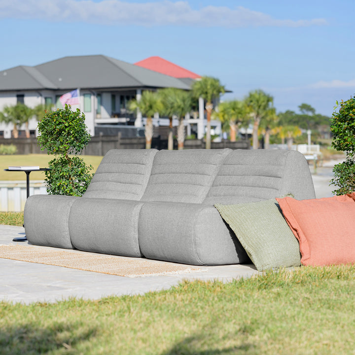 Gray outdoor sofa with colorful cushions on a patio with a house and trees in the background #color_port-gray-outdoor-performance-linen