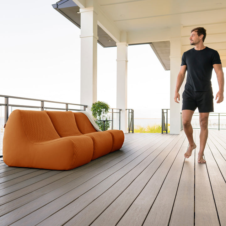 Man walking on a wooden deck with an orange outdoor sofa #color_honey-sand-outdoor-vegan-leather