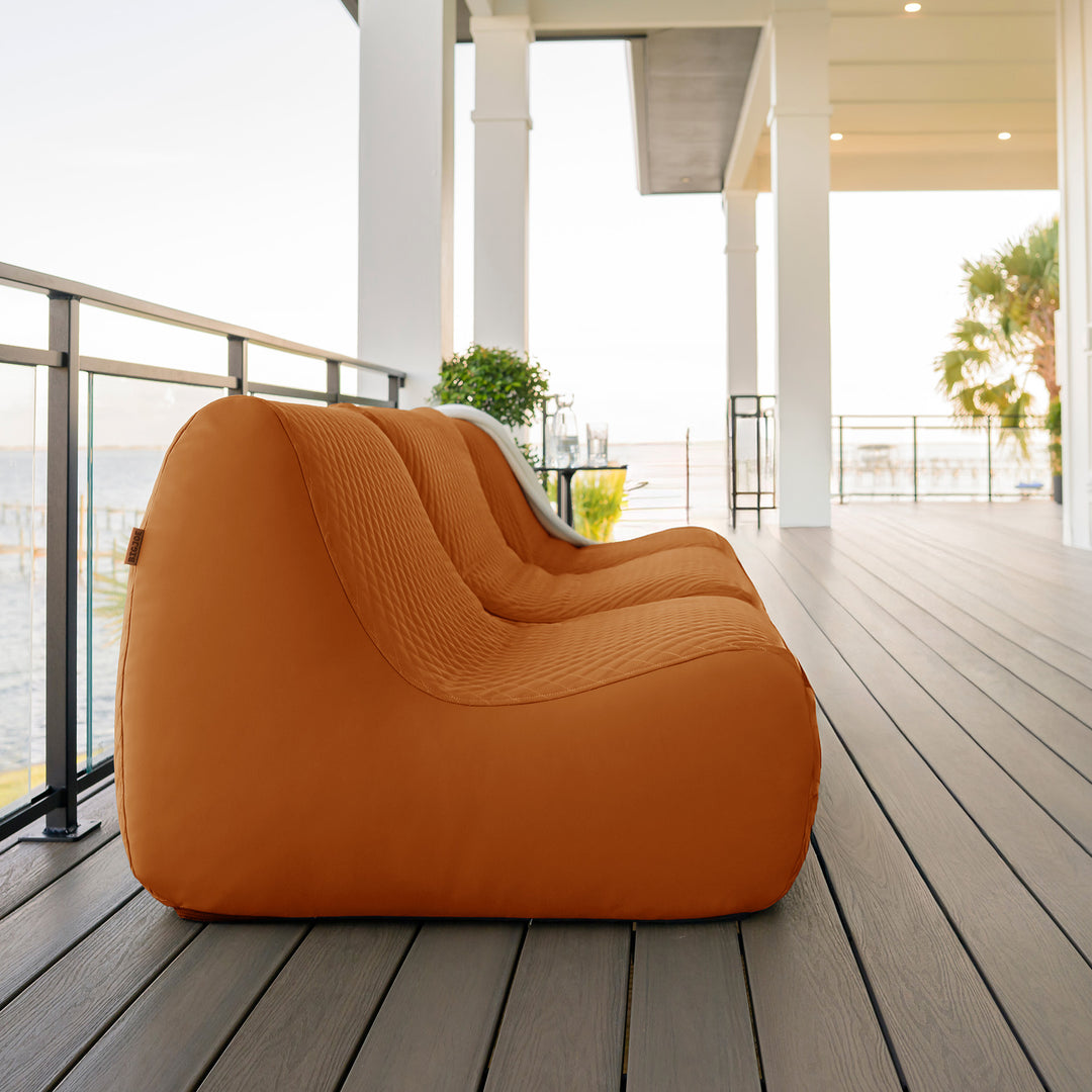 Orange sofa on a wooden deck with a modern house in the background #color_honey-sand-outdoor-vegan-leather
