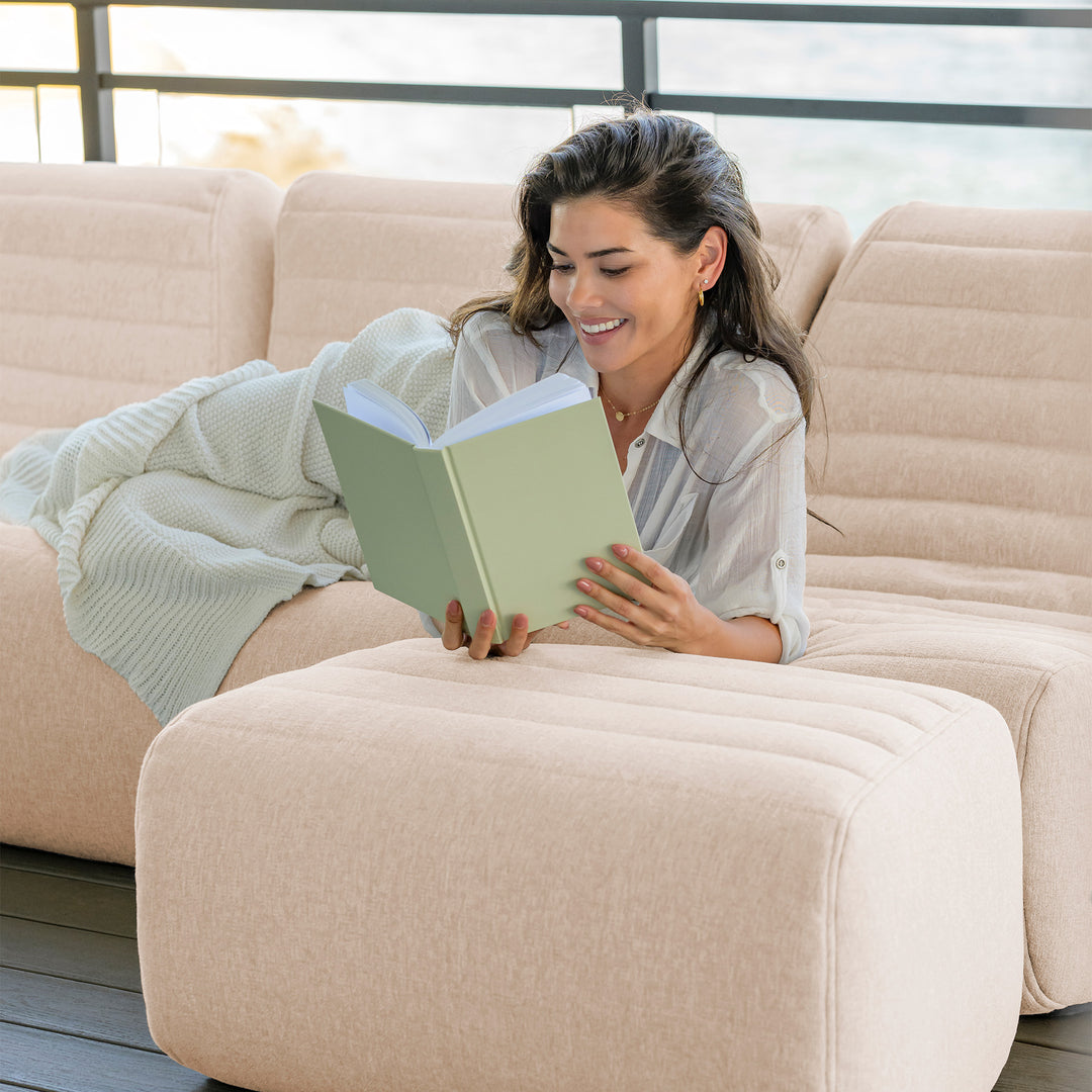 Woman reading a book on a beige sofa in a bright room #color_sunlit-cream-outdoor-performance-linen