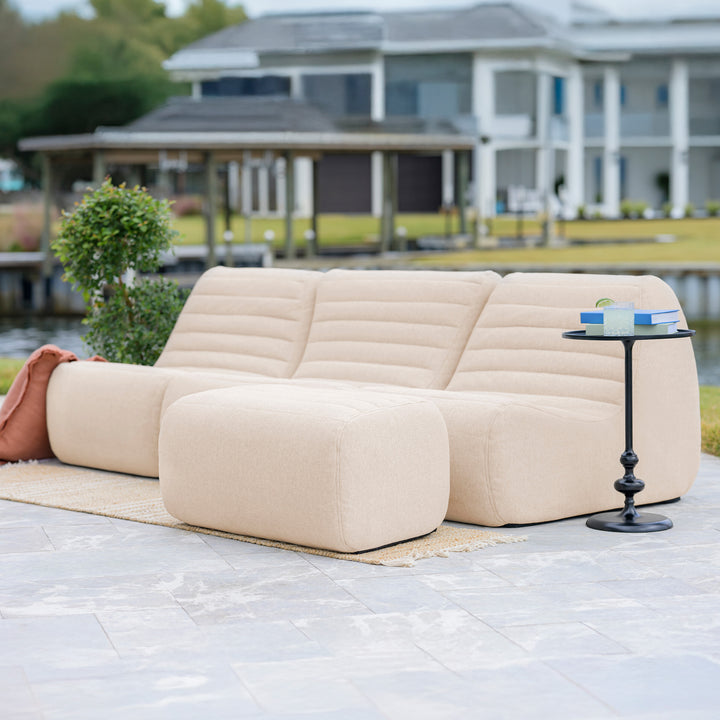 Beige outdoor sofa with a small table on a patio area with a waterfront background #color_sunlit-cream-outdoor-performance-linen