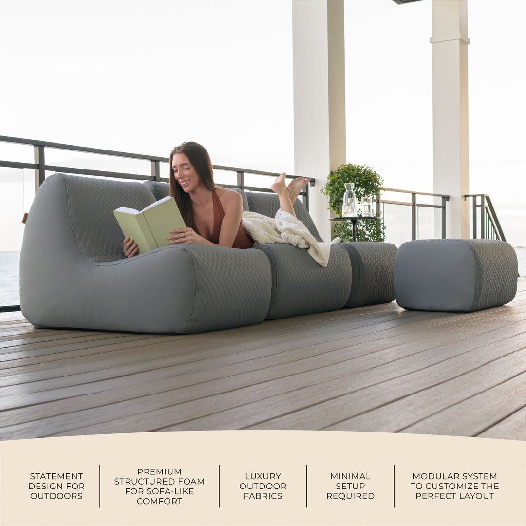 Woman reading a book on a modern outdoor sofa with text about product features. #color_moonlit-gray-outdoor-vegan-leather